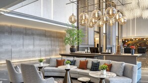 A modern lobby with a grey sofa, armchairs, and a coffee table. There is a reception desk with a plant and decorative items.