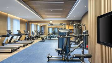 Un gimnasio con cintas de correr, máquinas de pesas y una pantalla de televisión.