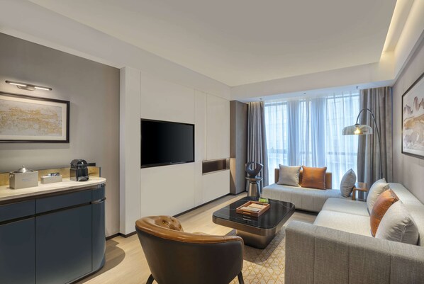 A modern hotel room with a flat-screen TV, a sofa, a coffee table, and a desk with a lamp. - Wyndham Xiong'An (Baoding)