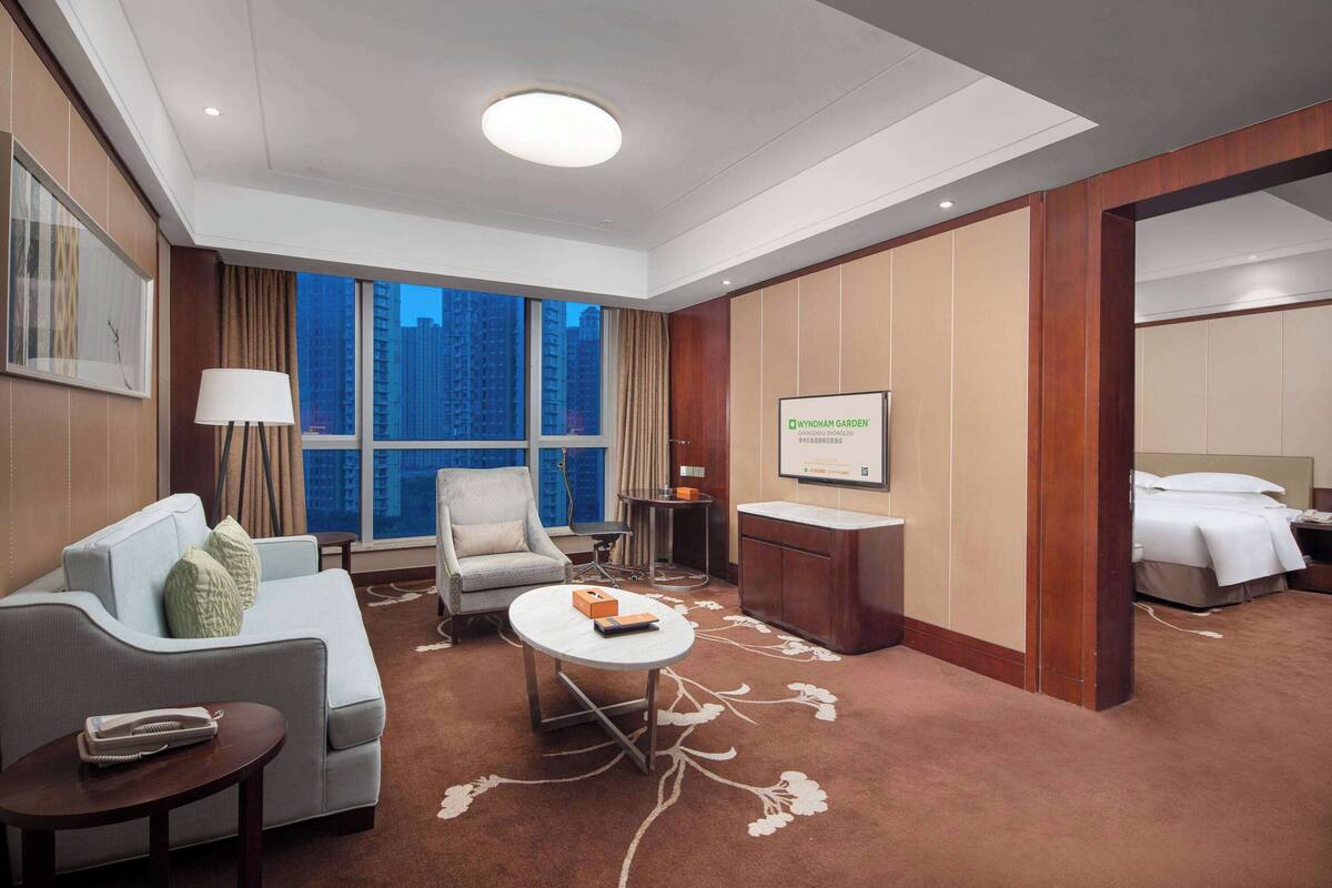 A hotel room with a sofa, armchair, small table, and a bed.