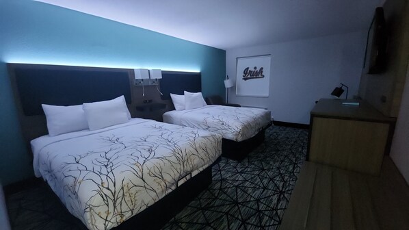 Une chambre d’hôtel avec deux lits, un bureau et un téléviseur fixé au mur.