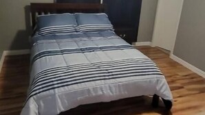 Ein Schlafzimmer mit Holzboden, einem Bett mit gestreifter Bettwäsche, einem Deckenventilator und dunklen Vorhängen.