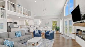 A spacious living area with a high ceiling, a balcony, and a kitchen in the background. - Lagoon Front | Private Pool and Pier | Pet Friendly (Gulf Shores)