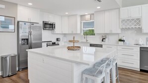 A modern kitchen with white cabinetry, stainless steel appliances, and a central island with bar stools. - Lagoon Front | Private Pool and Pier | Pet Friendly (Gulf Shores)
