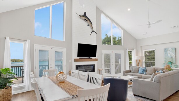 A spacious living area with a dining table, white chairs, a grey sofa, and a television. - Lagoon Front | Private Pool and Pier | Pet Friendly (Gulf Shores)