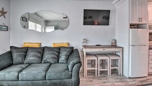 Un soggiorno con un divano grigio, una scrivania in legno, un armadietto bianco e un grande specchio appeso al muro.