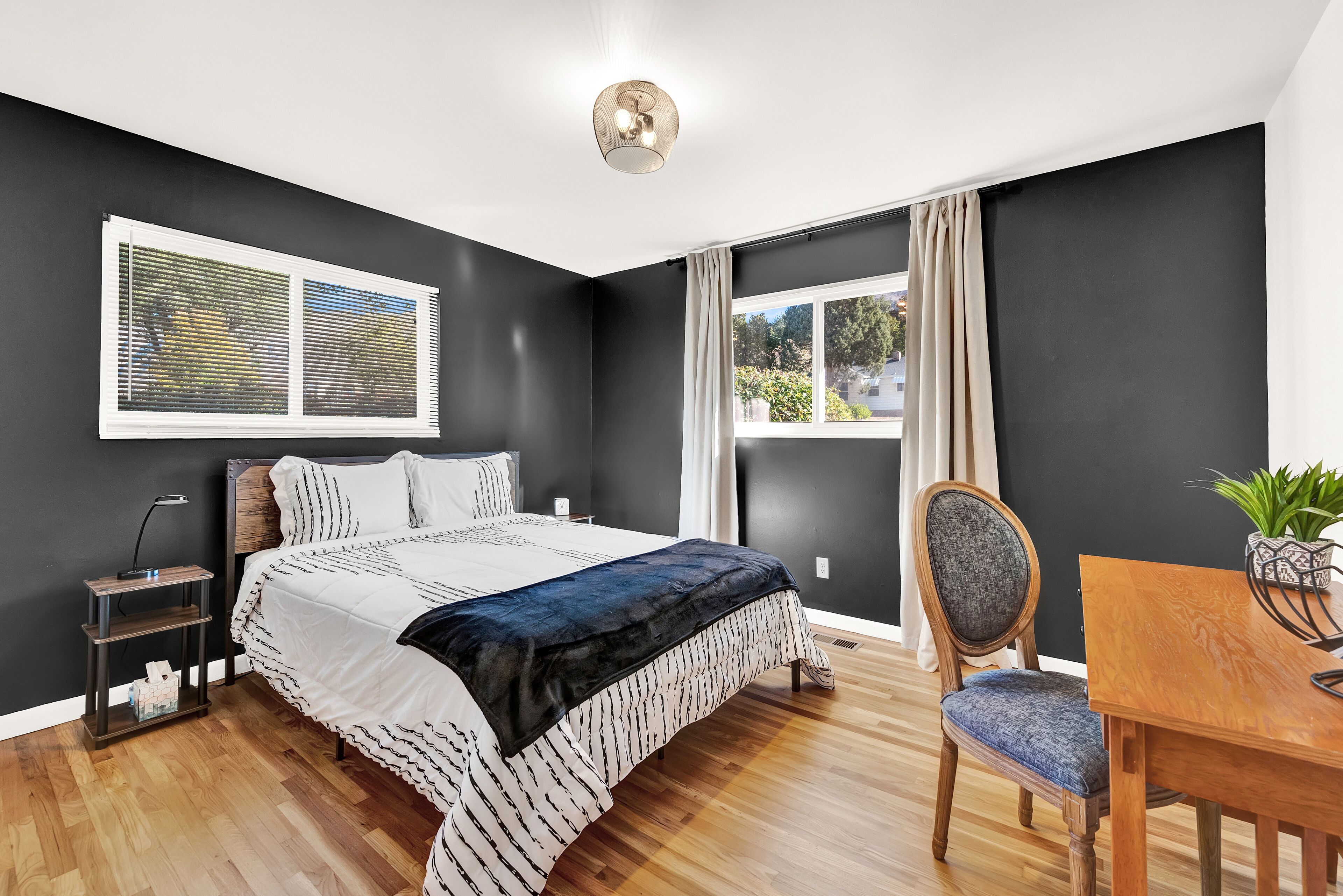 Une chambre à coucher avec un lit, une table de chevet, une lampe et une fenêtre avec des rideaux.