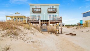 Une propriété située en bord de mer, avec un bâtiment à deux étages doté de balcons et d’une terrasse en bois.