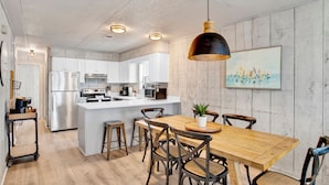 Une cuisine moderne avec des meubles blancs, des appareils en acier inoxydable et une table à manger en bois, accompagnée de chaises.