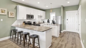 Una cocina moderna con armarios blancos, encimeras de granito y una isla central con taburetes de bar.