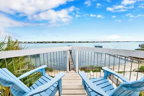A deck with blue chairs overlooking a body of water, a pier, and distant buildings.