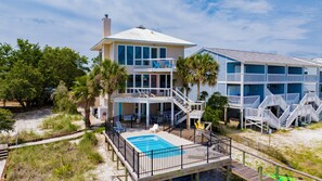 A multi-story beachfront property with a pool, outdoor seating, and a staircase leading to the upper levels.