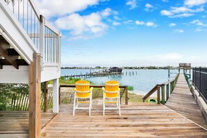 A wooden deck with two chairs facing a body of water, a dock, and a building with a railing.