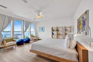A bedroom with a bed, a ceiling fan, a view of the water, and a bookshelf.