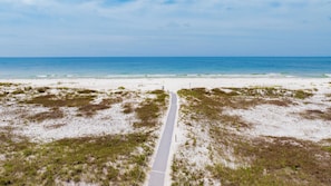 A beach with a pathway leading to the water, sandy dunes, and a clear sky.