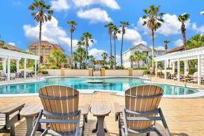 A pool area with lounge chairs and a table, surrounded by palm trees and buildings. - Luxury Retreat | Private Pool | Resort Style Amenities (Gulf Shores)