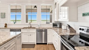 A kitchen with white cabinets, a stainless steel dishwasher, a stove, and a view of the outdoors. - Luxury Retreat | Private Pool | Resort Style Amenities (Gulf Shores)
