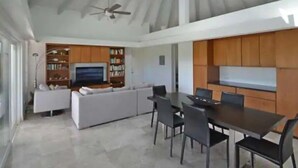A spacious living area with a high ceiling, a ceiling fan, a television, a sofa, a dining table with chairs, and built-in wooden cabinets. - Breezy, eco-friendly, with pool and lagoon view (Caicos Islands)