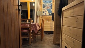 Un intérieur en bois comprenant un coin repas, un porte-manteau fixé au mur et une porte dotée d’un panneau en bois.