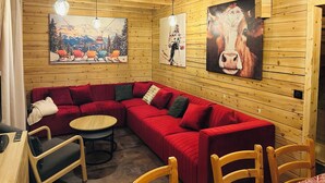 Une pièce chaleureuse avec un canapé d’angle rouge, une petite table ronde et des murs en bois ornés de tableaux.