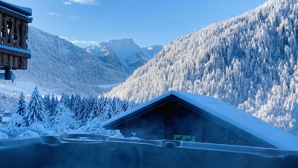Une cabane en bois, dotée d’un toit en pente, entourée d’arbres et de montagnes couverts de neige.