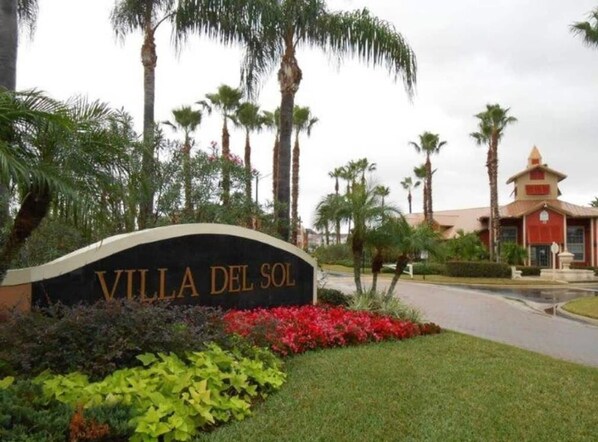 A sign for Villa Del Sol with a landscaped garden and palm trees.