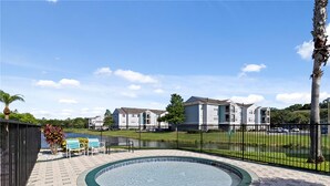 A swimming pool with a tiled deck, surrounded by a fence, and a view of residential buildings in the background. - Very Nice apartment , near to Disney (Kissimmee)