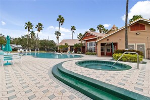A pool area with two pools, lounge chairs, and a building with a red roof.