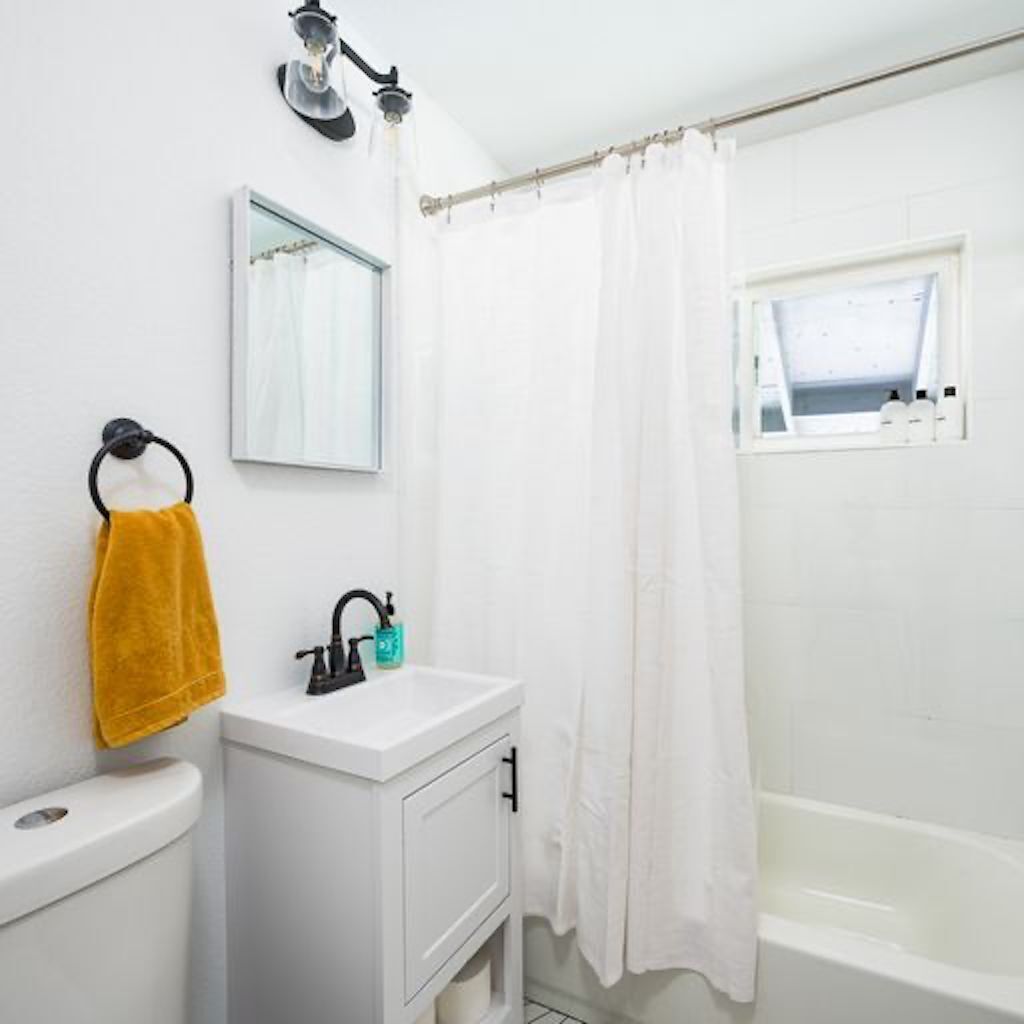A bathroom with a white sink, a yellow towel, a black faucet, and a white bathtub.