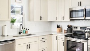 A modern kitchen with white cabinets, a stainless steel oven, a microwave, and a black kettle on the stove. - Bright & Modern Retreat - Sleeps 8 - Convenient Location (Wheat Ridge)