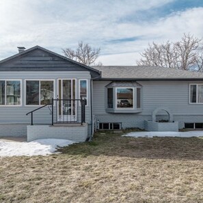 A two-story house with a front porch, a small attached garage, and a snow-covered lawn. - Bright & Modern Retreat - Sleeps 8 - Convenient Location (Wheat Ridge)