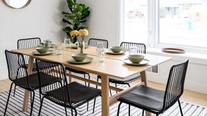A dining area with a wooden table, black chairs, a hanging light fixture, a mirror, and a window with a view of the outside. - Bright & Modern Retreat - Sleeps 8 - Convenient Location (Wheat Ridge)