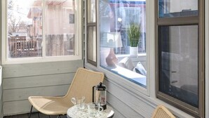 A small, enclosed porch with wicker chairs and a table, large windows, and a view of the street. - Bright & Modern Retreat - Sleeps 8 - Convenient Location (Wheat Ridge)
