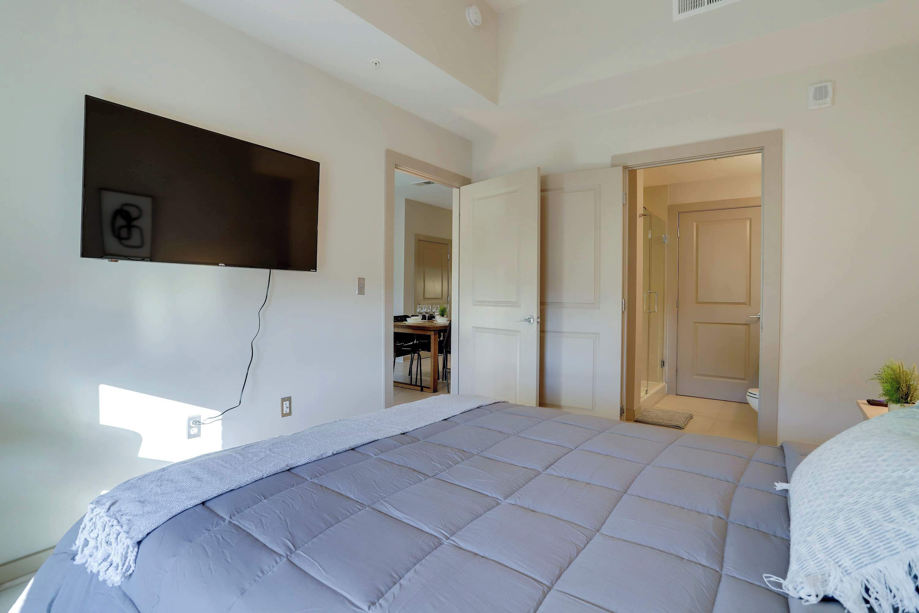 Un dormitorio con cama, televisión montada en la pared y puerta que da a un baño.