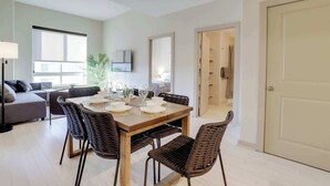 A dining area with a wooden table and wicker chairs, a sofa, and a TV mounted on the wall. - Stylish Comfort Meets Spacious Design (Arlington)