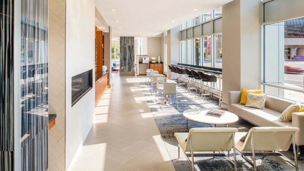 A modern hotel lobby with a long reception desk, seating area with tables and chairs, and large windows offering views of the outside. - Stylish Comfort Meets Spacious Design (Arlington)