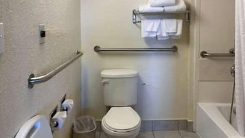 A bathroom with a toilet, a handrail, a trash bin, and a towel rack.
