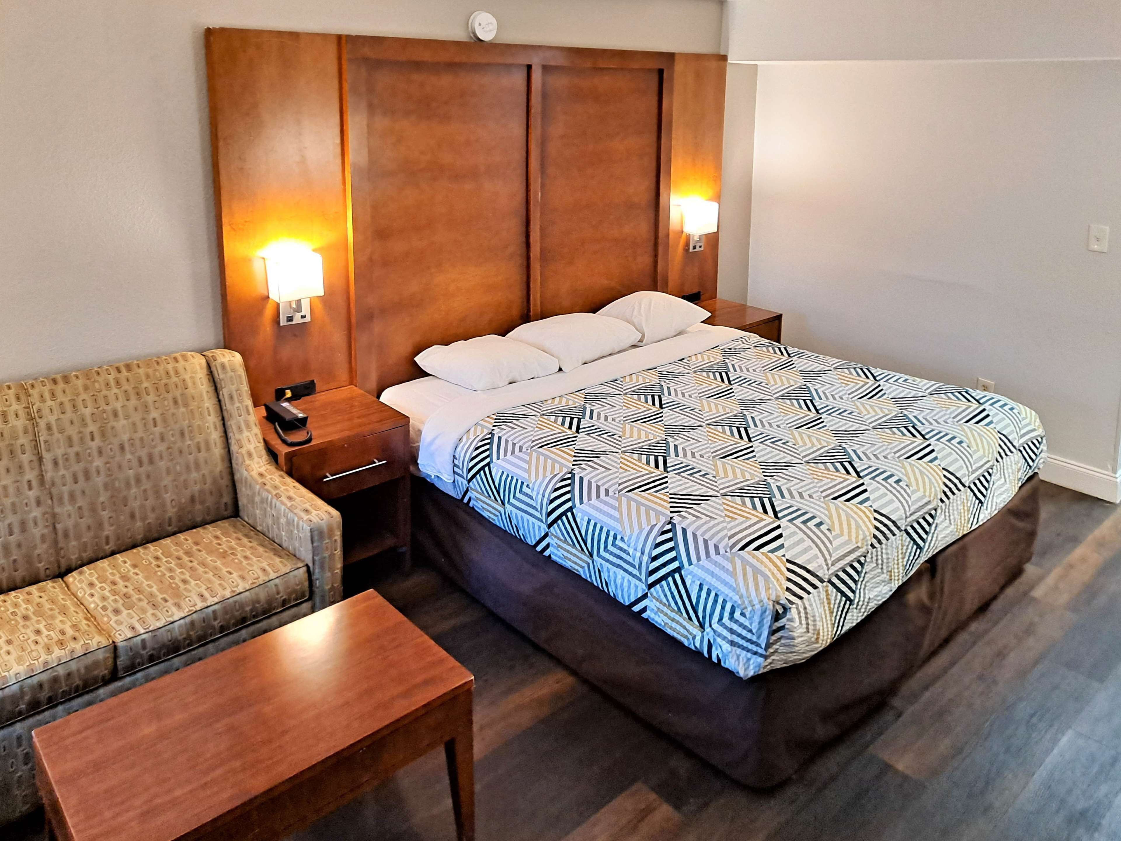 Una habitación de hotel con una cama, un sofá, una mesita de noche y una pequeña mesa.