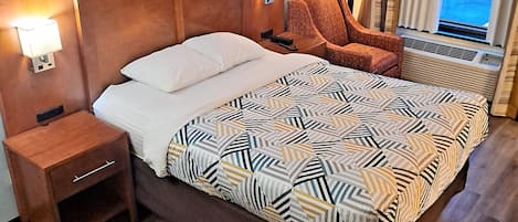 A hotel room with a large bed, a nightstand, a chair, and a window with curtains.