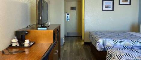 A hotel room with a wooden desk, a television, a bed with patterned bedding, and two framed pictures on the wall.