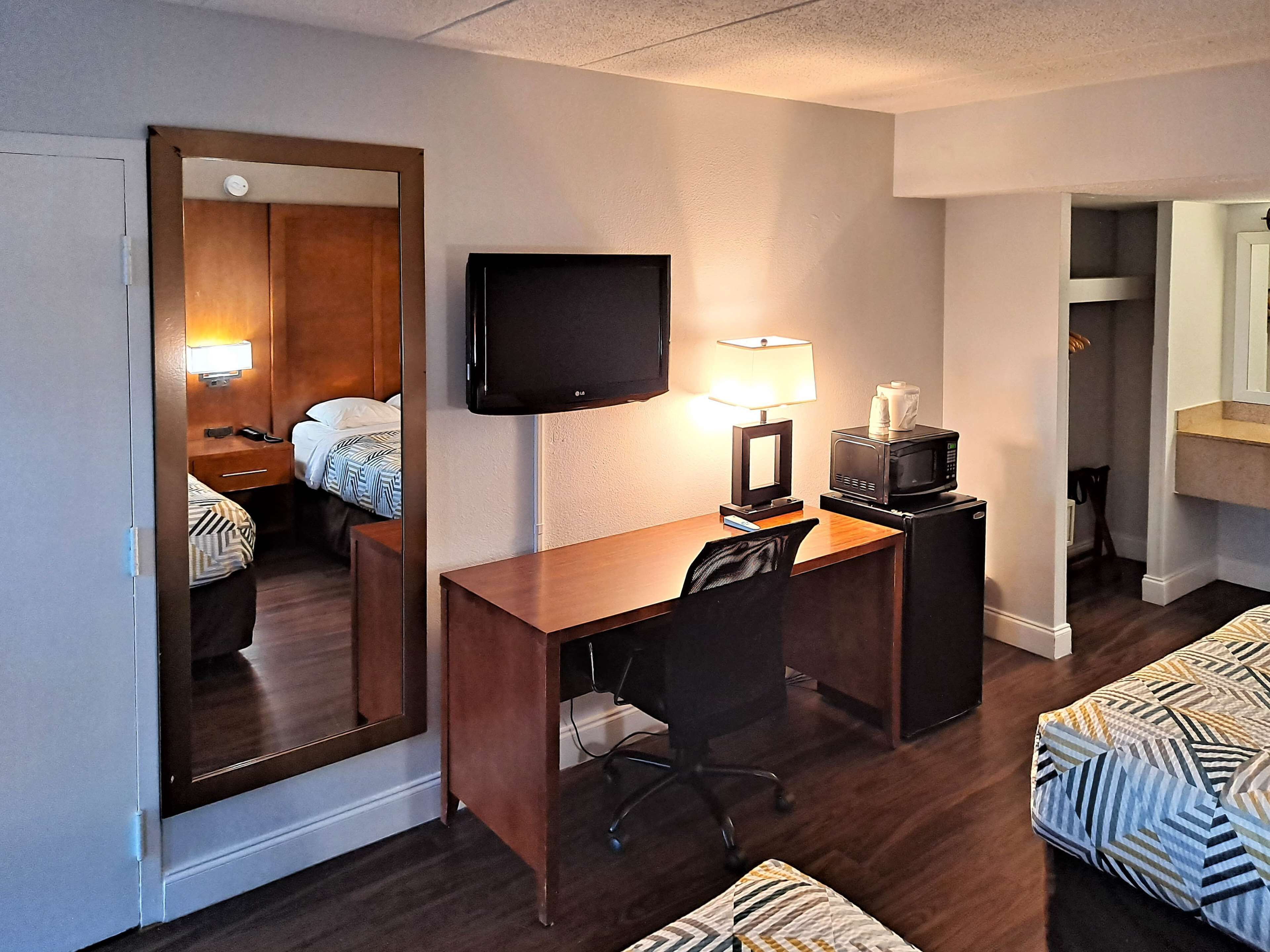 Une chambre d’hôtel avec un bureau en bois, une télévision, une lampe, un four à micro-ondes, un lit avec une literie à motifs et un miroir.