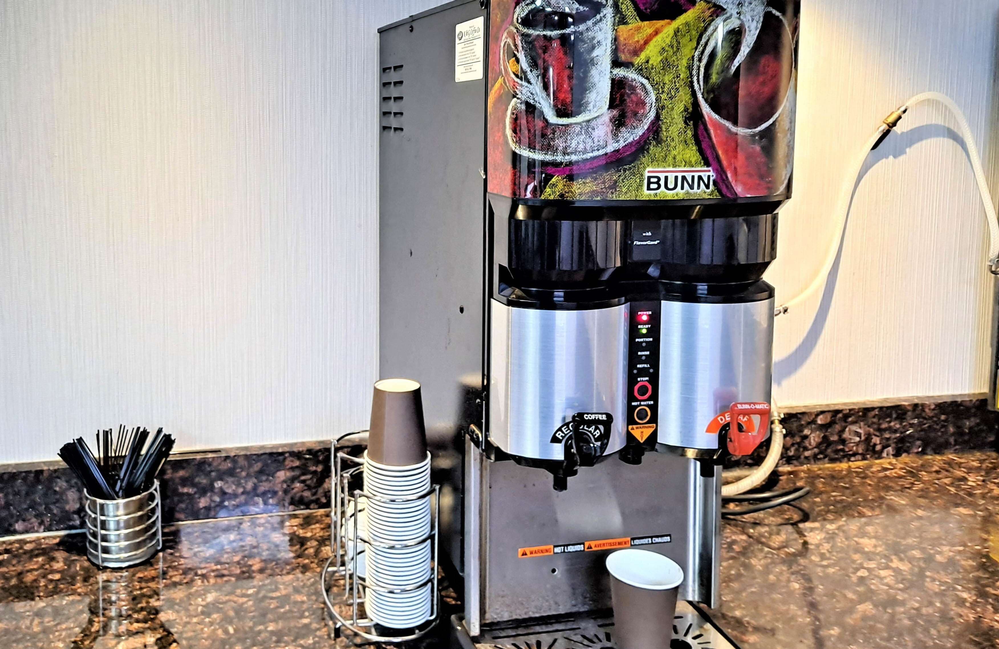 A coffee machine with a Bunn logo, a cup holder, and a stack of disposable cups on a countertop.
