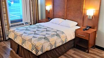 Habitación de hotel con una cama grande, cabecera de madera, dos mesitas de noche con lámparas y vista a un estacionamiento a través de una ventana.
