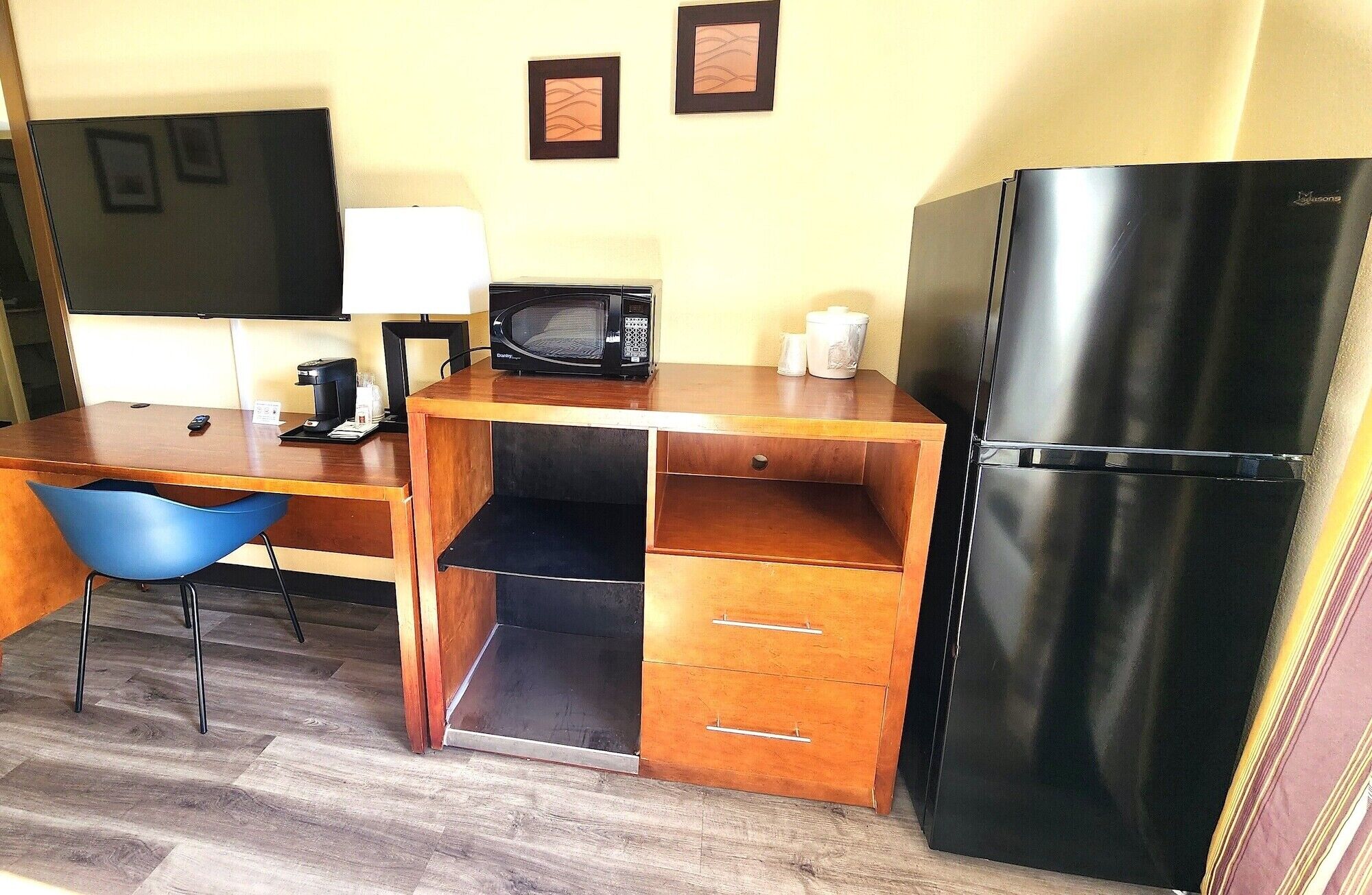 Una kitchenette compacta con microondas, cafetera, refrigerador y una silla azul.