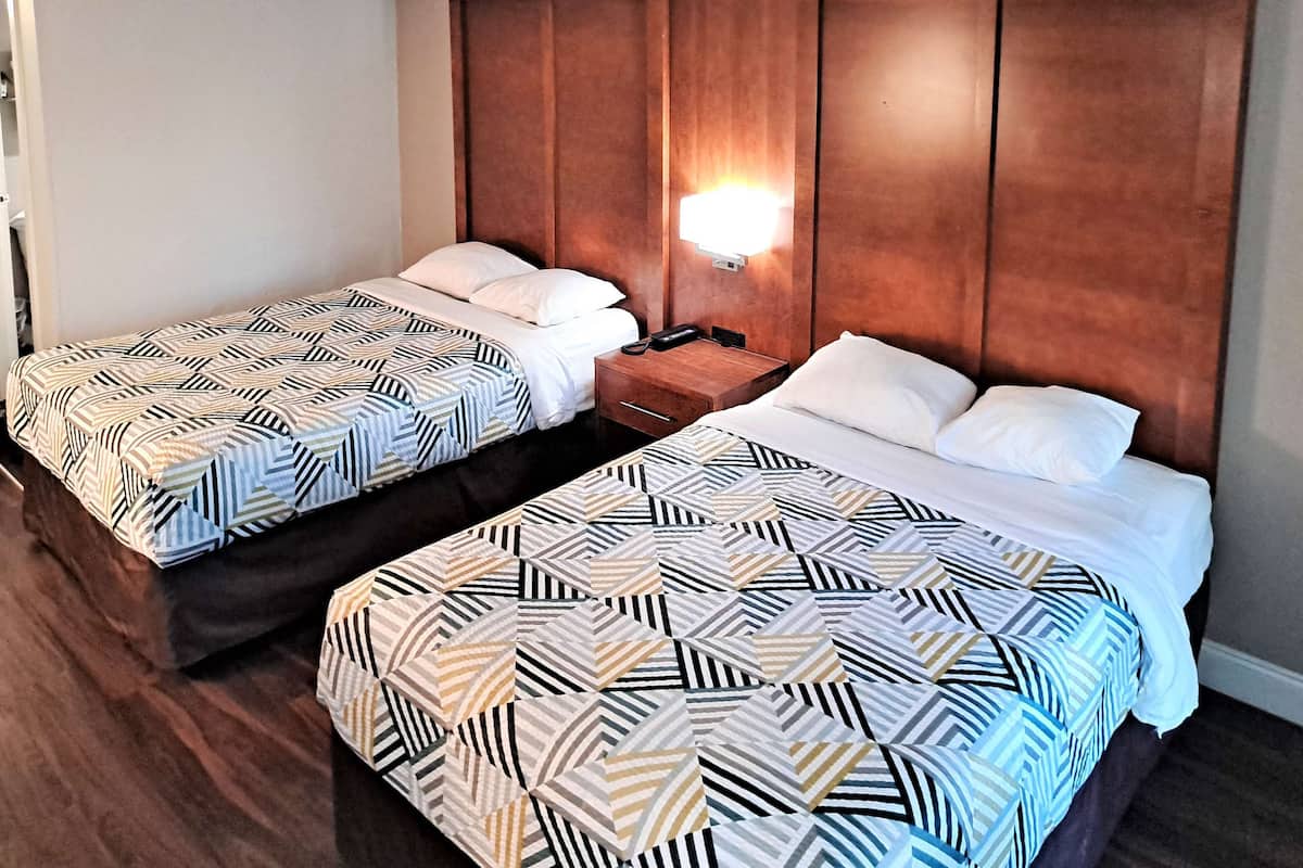 Habitación de hotel con dos camas, cada una con ropa de cama estampada, cabeceros de madera y una mesita de noche con lámpara.