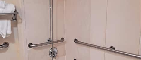 Une salle de bain avec une baignoire blanche, des barres d’appui, une pomme de douche et un porte-serviettes.