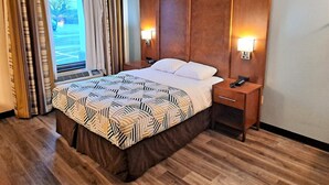 A hotel room with a large bed, wooden headboard, two bedside tables with lamps, a window with curtains, and a view of the outdoors. - Studio 6 Suites Catonsville, Md – Baltimore West (Catonsville)