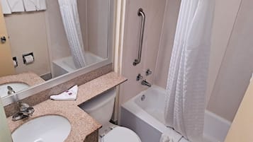 Un baño con lavamanos, inodoro y bañera. Hay un pasamanos en la zona de la ducha.