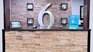 A reception desk with a large '6' sign, a computer, a phone, and a promotional sign. - Studio 6 Suites Catonsville, Md – Baltimore West (Catonsville)
