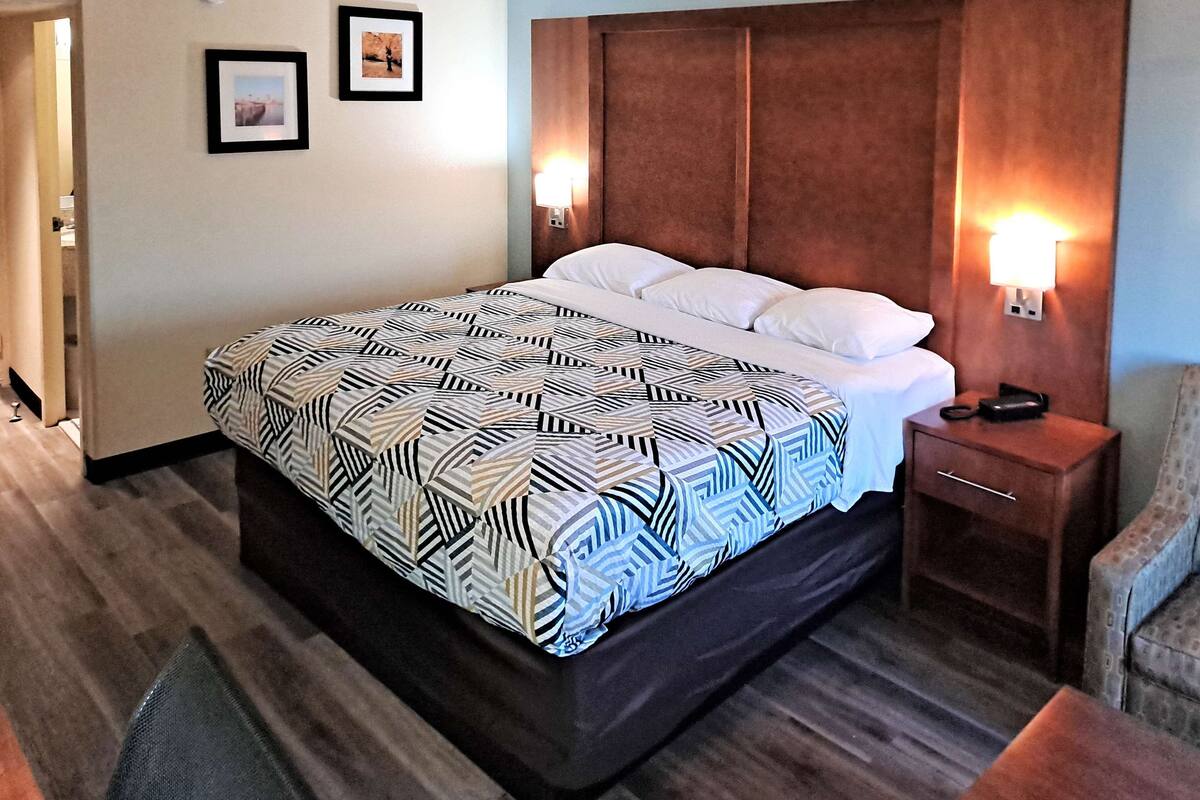 Habitación de hotel con una cama grande, dos mesitas de noche, una silla y una lámpara de pared.